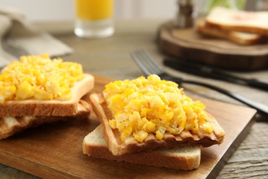 Delicious breakfast with scrambled eggs and toasted bread served on wooden board, closeup