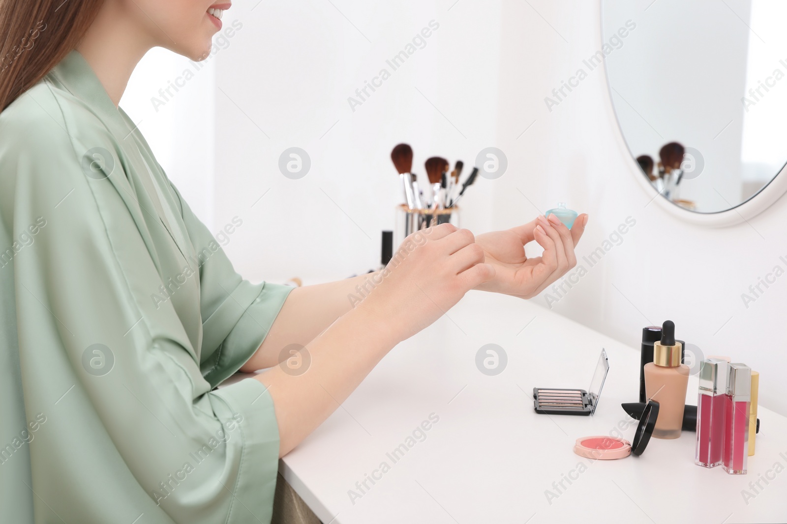 Photo of Woman applying perfume on wrist at dressing table indoors, closeup