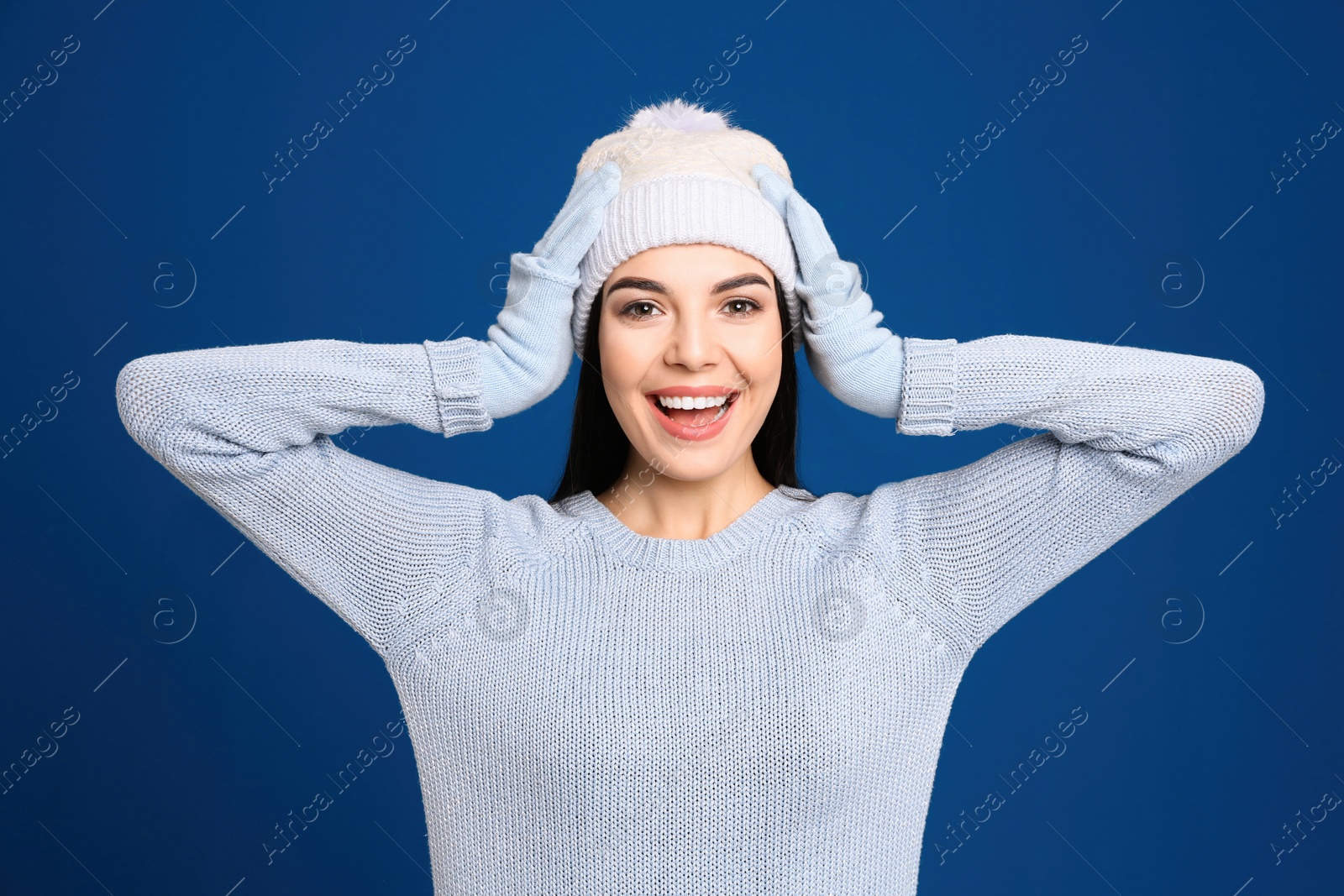 Photo of Young woman wearing warm sweater, gloves and hat on blue background. Winter season