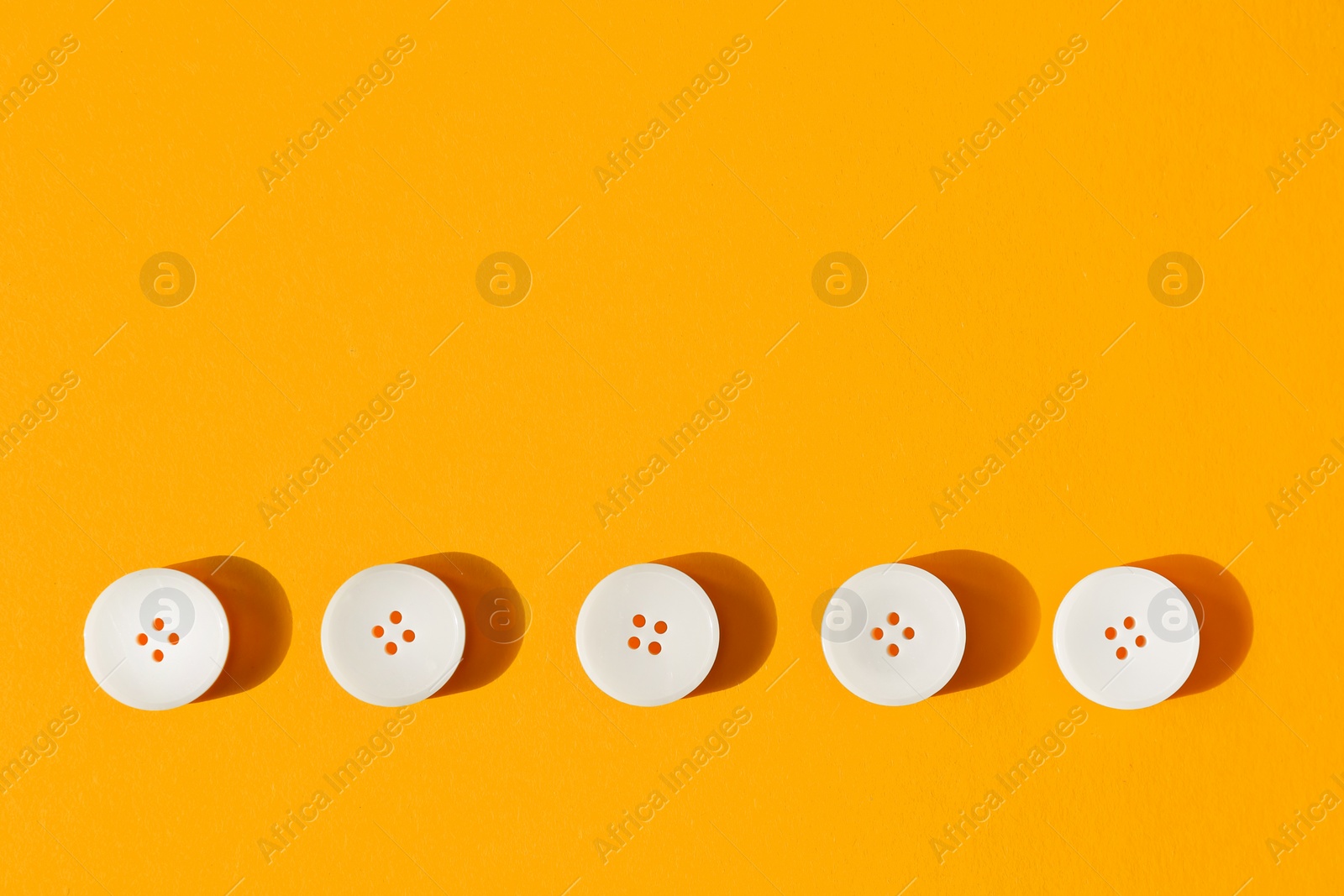 Photo of Line of white buttons on orange background, flat lay. Space for text