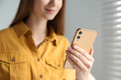 Young woman using modern smartphone indoors, closeup