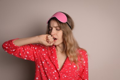Photo of Young tired woman with sleeping mask yawning on beige background