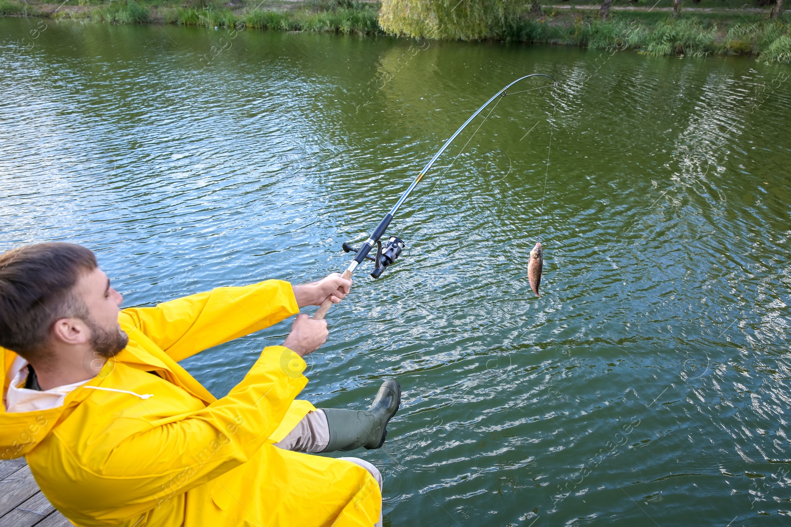 Photo of Man with rod fishing on wooden pier at riverside. Recreational activity