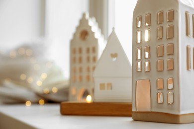 Beautiful house shaped candle holders and festive lights on windowsill indoors, closeup. Space for text