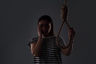 Depressed woman with rope noose on grey background