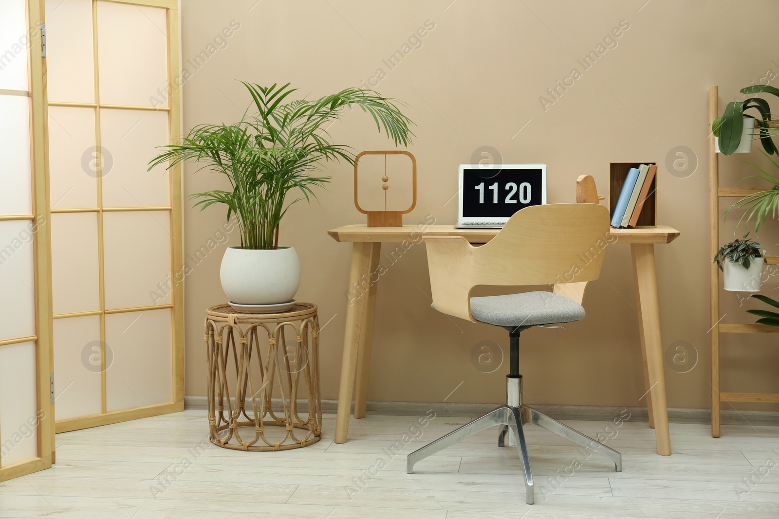Photo of Stylish workplace with laptop, armchair and houseplants in room. Interior design