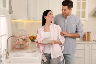 Photo of Happy couple with clean dishes in kitchen