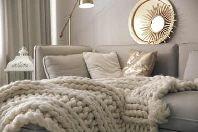 Warm knitted blanket on grey sofa in living room. Interior design