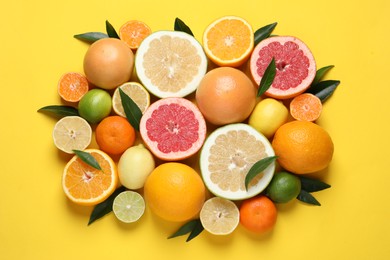 Photo of Different ripe citrus fruits with green leaves on yellow background, flat lay