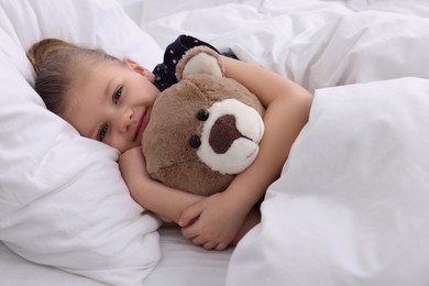 Photo of Cute little girl lying with teddy bear in bed