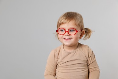 Photo of Cute little girl in glasses on light grey background. Space for text