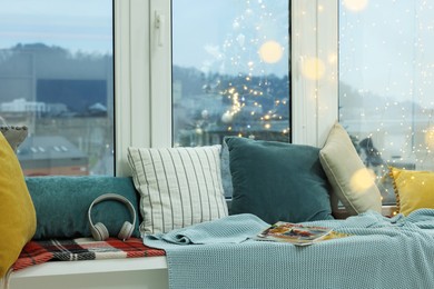 Photo of Cosy window sill with pillows, blanket and festive lights indoors. Interior design