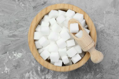 Photo of White sugar cubes in wooden bowl and scoop on grey table, top view