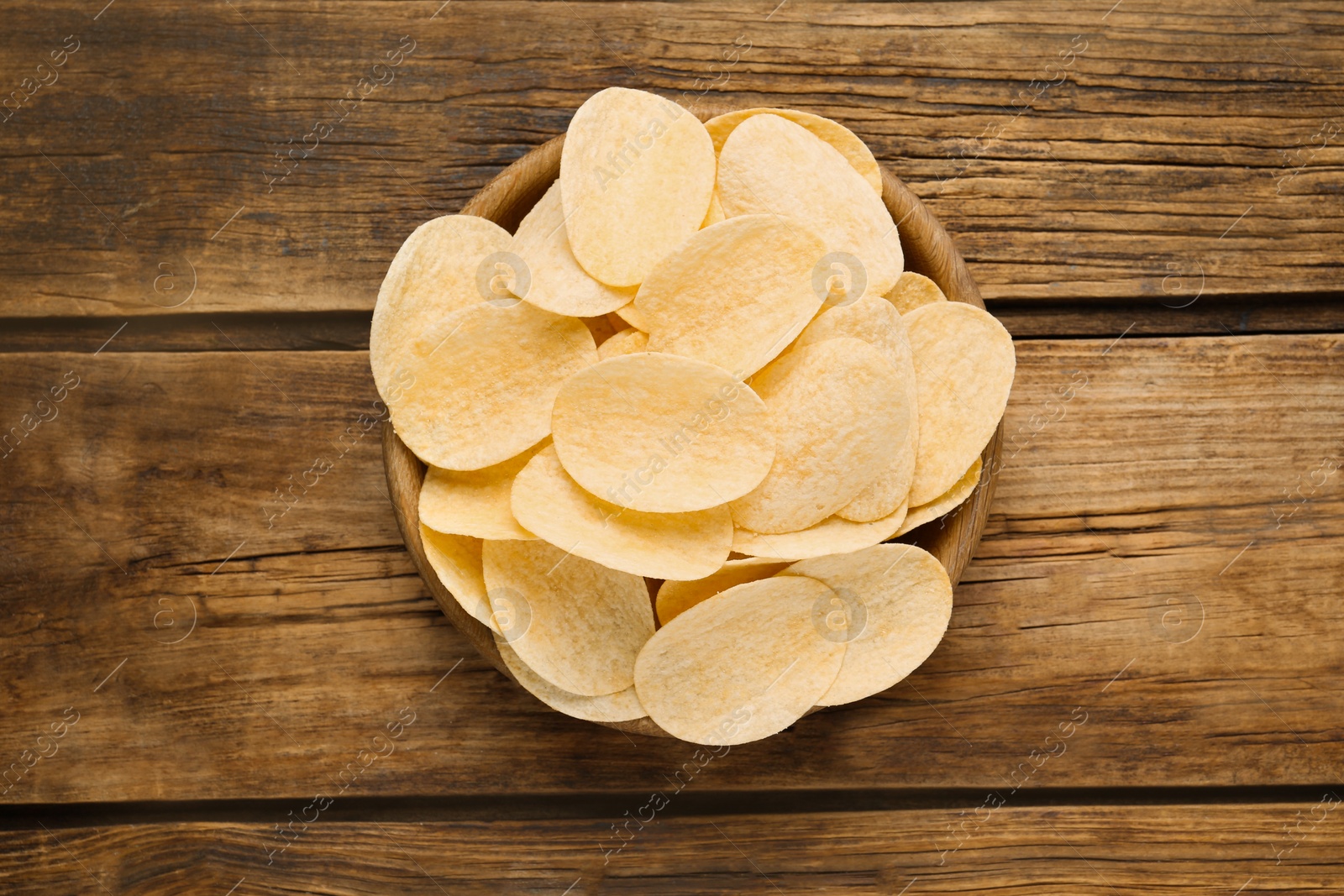 Photo of Bowl with delicious potato chips on wooden table, top view