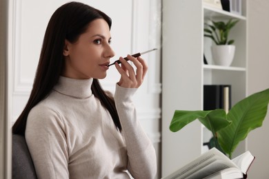 Woman using cigarette holder for smoking while reading book indoors