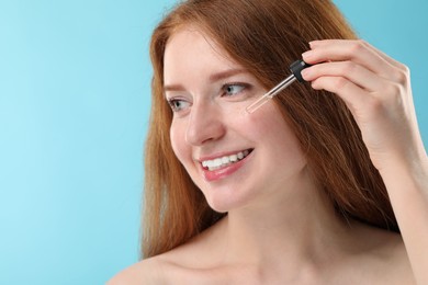 Photo of Smiling woman with freckles applying cosmetic serum onto her face against light blue background, closeup. Space for text