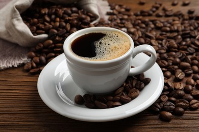 Cup of aromatic hot coffee and beans on wooden table