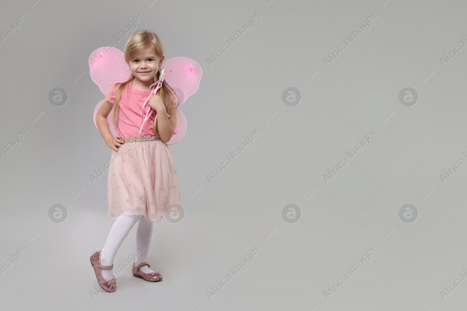 Photo of Cute little girl in fairy costume with pink wings and magic wand on light grey background, space for text