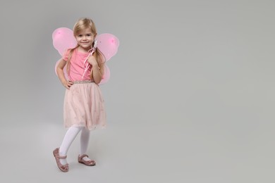 Photo of Cute little girl in fairy costume with pink wings and magic wand on light grey background, space for text