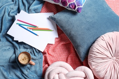 Photo of Flat lay composition with cup of coffee, pencils, pillows and plaid on bed