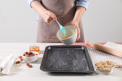 Photo of Making delicious baklava. Woman buttering baking pan at white wooden table, closeup