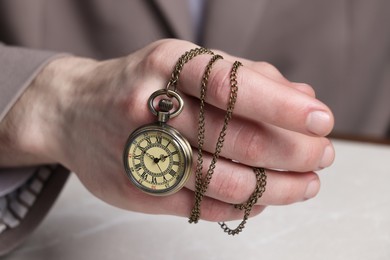 Man holding chain with elegant pocket watch at light marble table, closeup