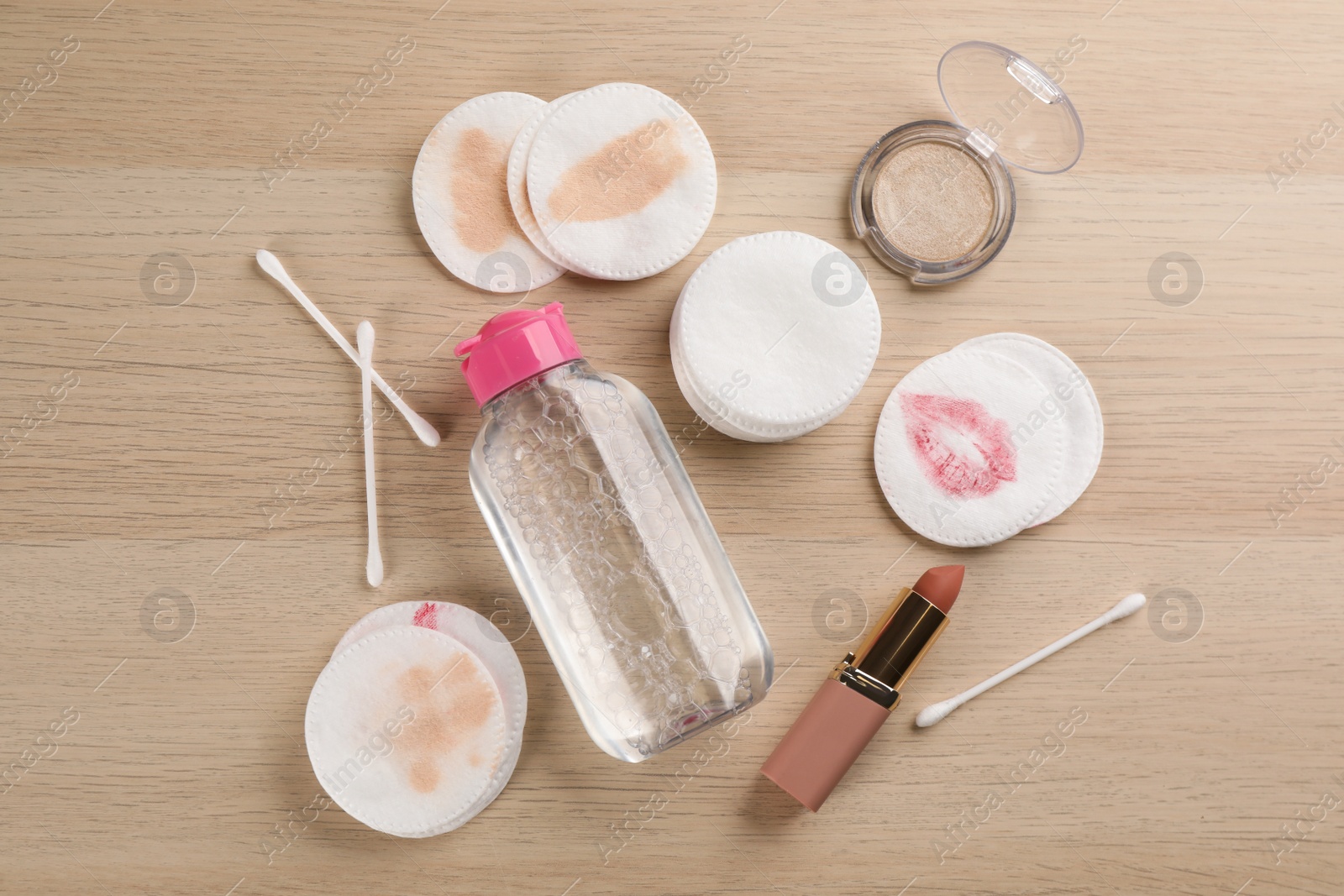 Photo of Dirty cotton pads, swabs, cosmetic products and micellar cleansing water on wooden background, flat lay