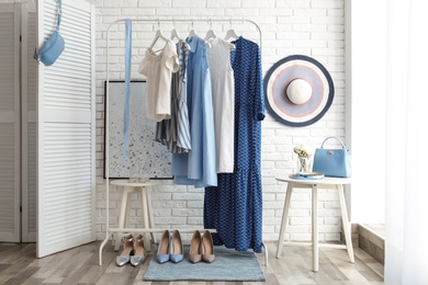 Wardrobe rack with women's clothes and different shoes at white brick wall in room