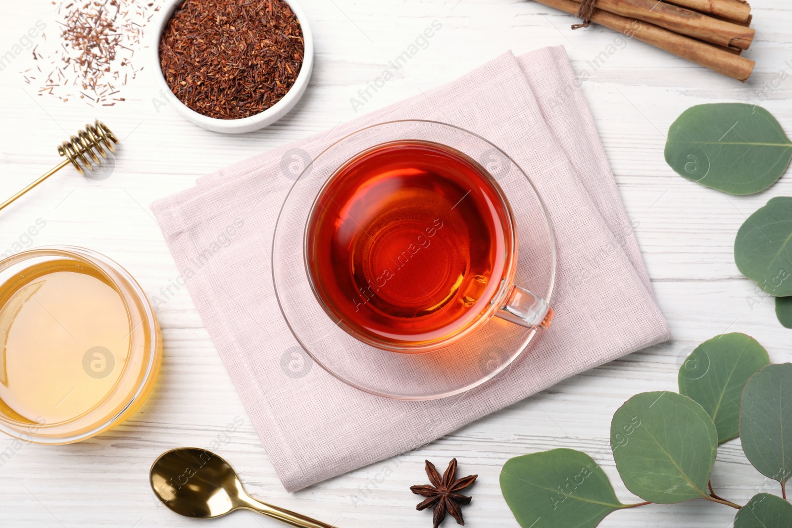 Photo of Freshly brewed rooibos tea, dry leaves, honey and spices on white wooden table, flat lay