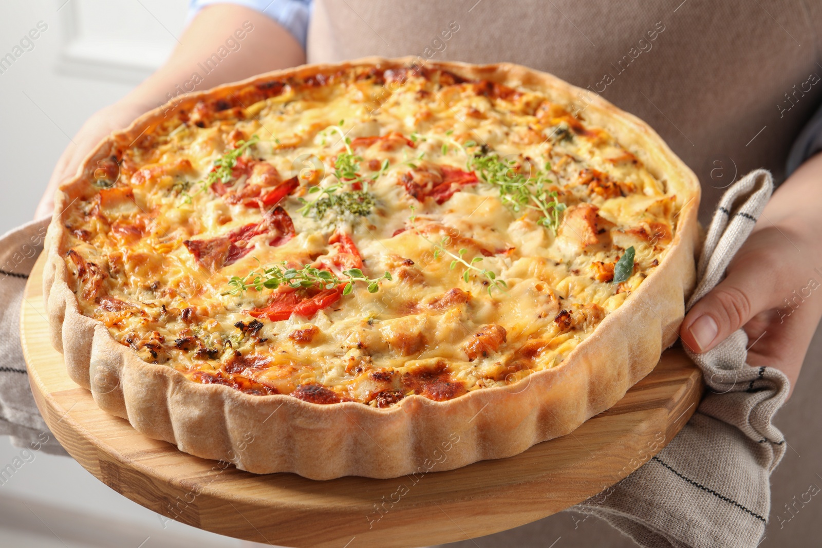 Photo of Woman holding board with tasty quiche indoors, closeup