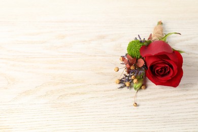 Stylish boutonniere with red rose on light wooden table. Space for text