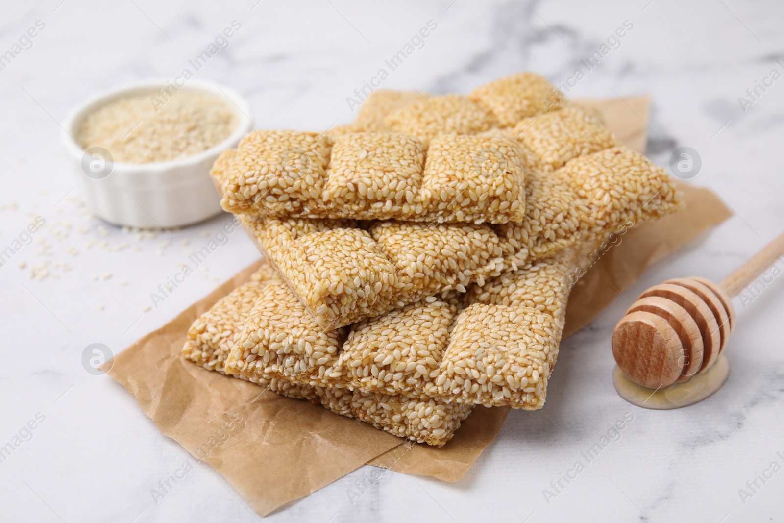 Photo of Delicious sweet kozinaki bars, sesame seeds and wooden dipper on white marble table, closeup