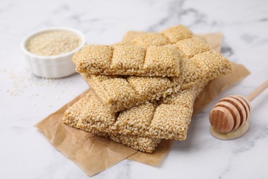 Photo of Delicious sweet kozinaki bars, sesame seeds and wooden dipper on white marble table, closeup