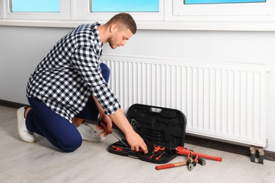 Photo of Professional plumber with different tools installing new heating radiator in room