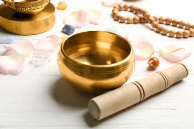 Photo of Composition with golden singing bowl and mallet on white wooden table. Sound healing