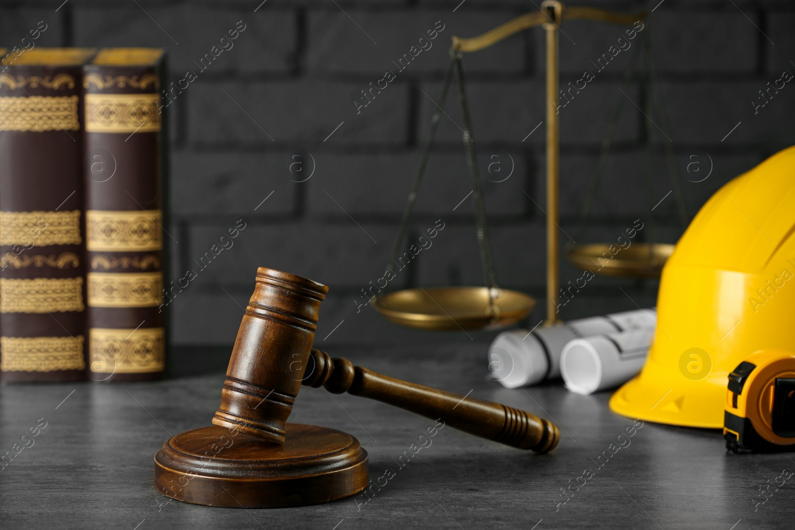 Photo of Construction and land law concepts. Judge gavel, books, protective helmet, scales of justice with drawings on grey table
