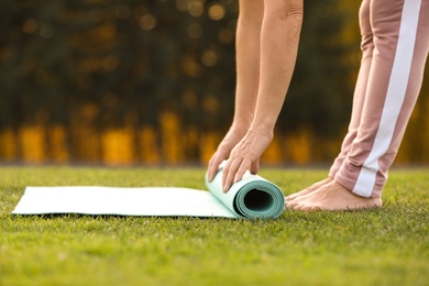 Photo of Mature woman unrolling yoga mat outdoors, closeup