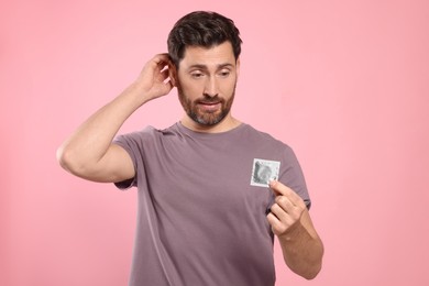 Photo of Confused man holding condom on pink background. Safe sex