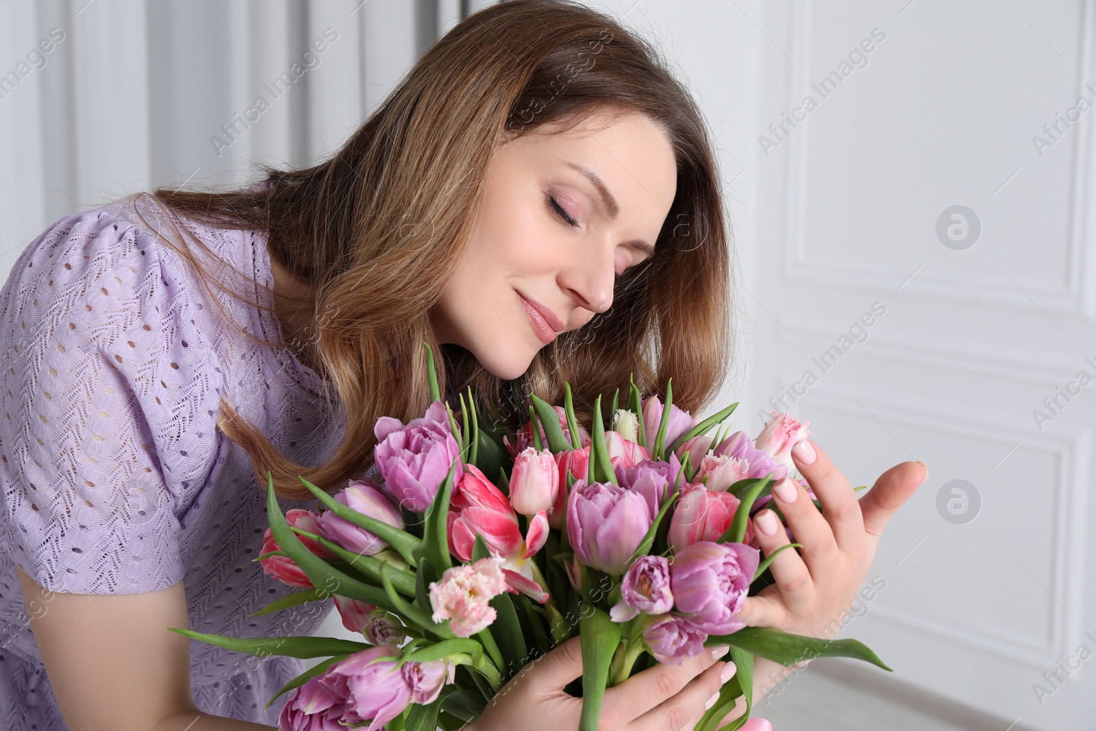 Photo of Young woman with bouquet of beautiful tulips indoors