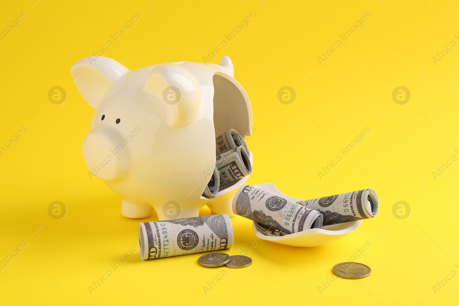 Photo of Financial savings. Broken piggy bank, dollar banknotes and coins on yellow background