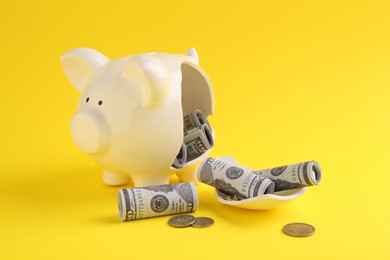 Financial savings. Broken piggy bank, dollar banknotes and coins on yellow background