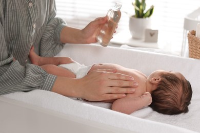 Photo of Mother massaging her cute baby with oil on changing table at home, closeup