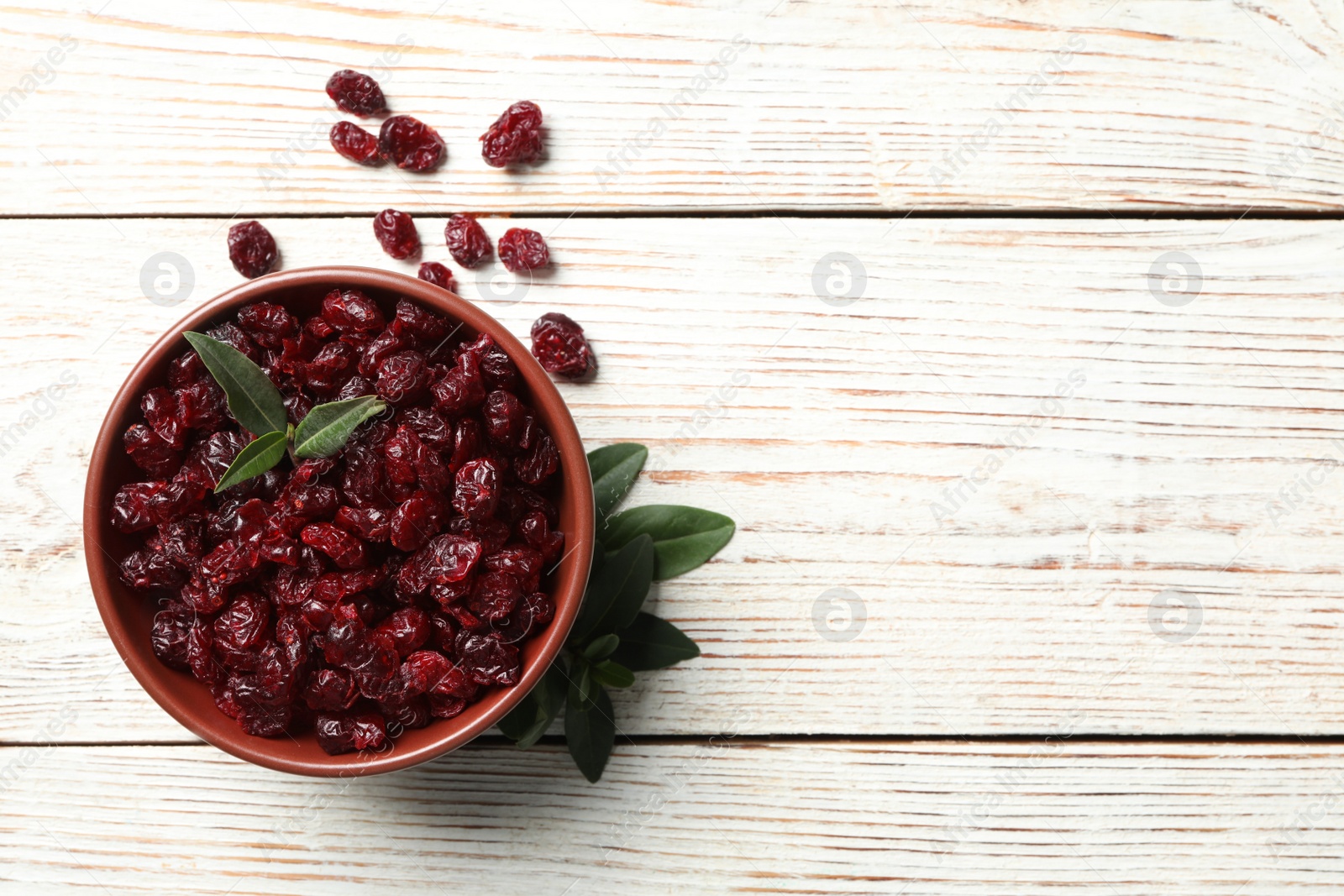 Photo of Tasty dried cranberries and leaves on white wooden table, flat lay. Space for text