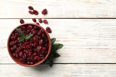 Photo of Tasty dried cranberries and leaves on white wooden table, flat lay. Space for text