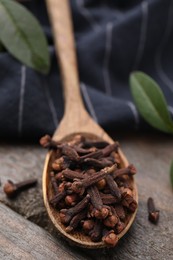 Spoon with aromatic cloves on wooden table, closeup