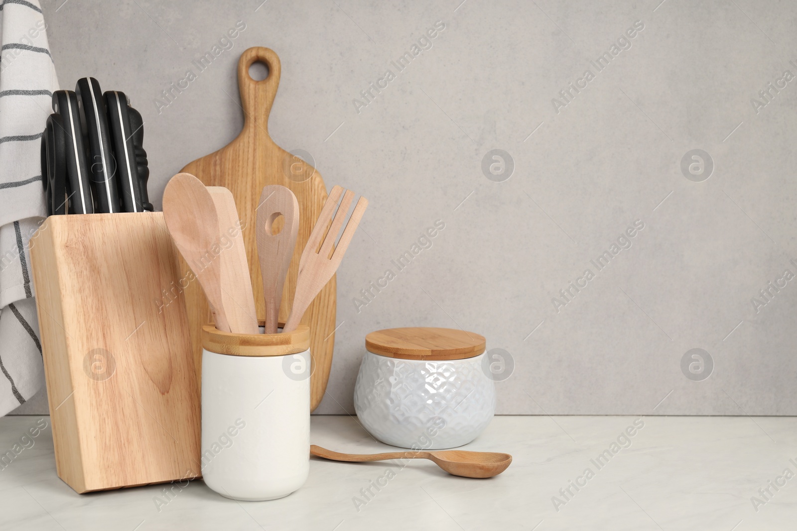 Photo of Set of different kitchen utensils on white near gray wall. Space for text