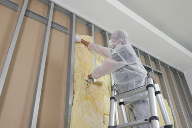 Photo of Worker insulating wall using ladder indoors, low angle view