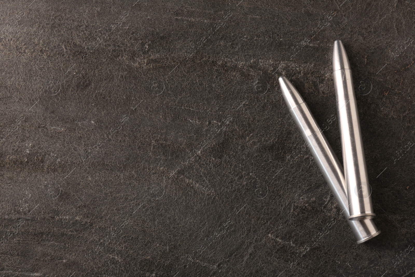 Photo of Metal bullets on dark textured table, flat lay. Space for text