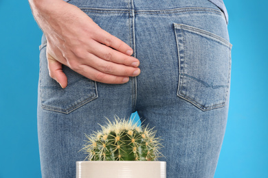 Photo of Man sitting down on cactus against light blue background, closeup. Hemorrhoid concept