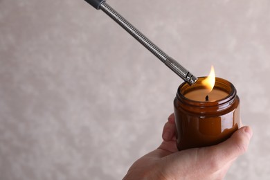 Photo of Woman lighting candle with gas lighter against grey wall, closeup